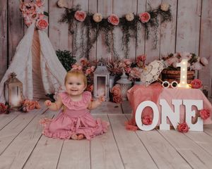 A series of connected milestone photos showing a baby growing up in a pink floral backdrop setting over their first year.