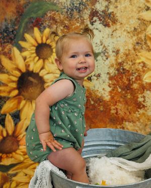 Infant playing with flour in a metal basin against an artistic autumn-toned background with sunflowers.