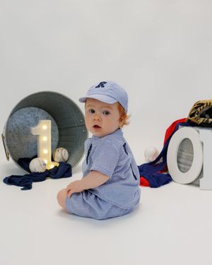 A baby in blue clothing crawls near decorative number one blocks placed on a white studio backdrop.