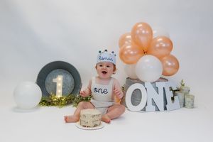 White cake smash decorations with elegant floral accents and peach balloons for a first birthday celebration setup.