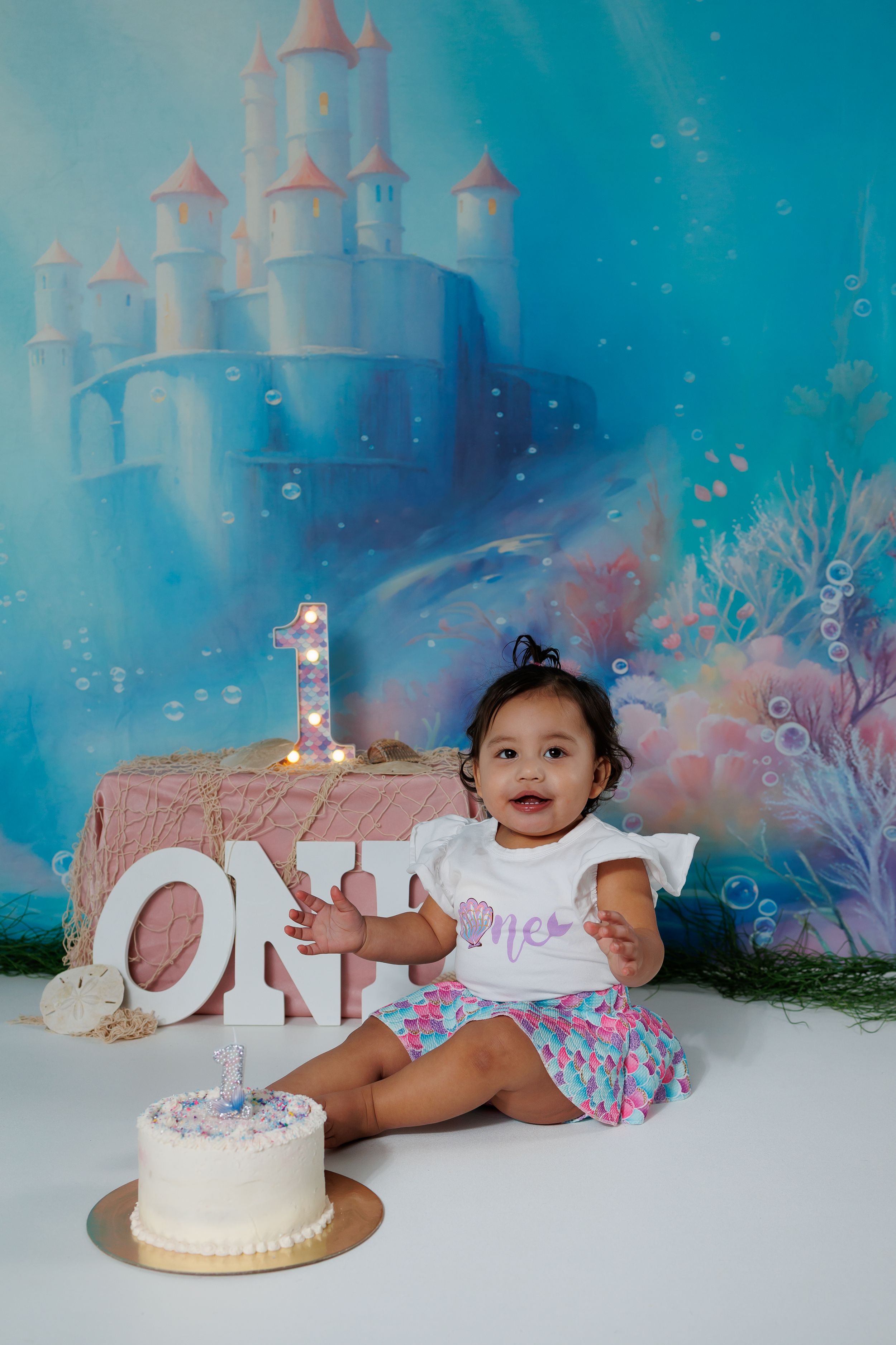 A cake smash photo session featuring a turquoise castle backdrop with magical lighting and bubbles.
