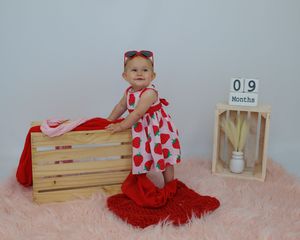 Red and white themed baby milestone photo setup with wooden crates and soft textiles against neutral background.