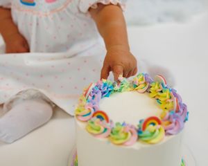 A rainbow-colored meringue cookie being decorated with colorful swirls and sprinkles on a white surface.