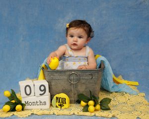 A series of five studio portraits with the same blue backdrop showing age progression from newborn to nine months.