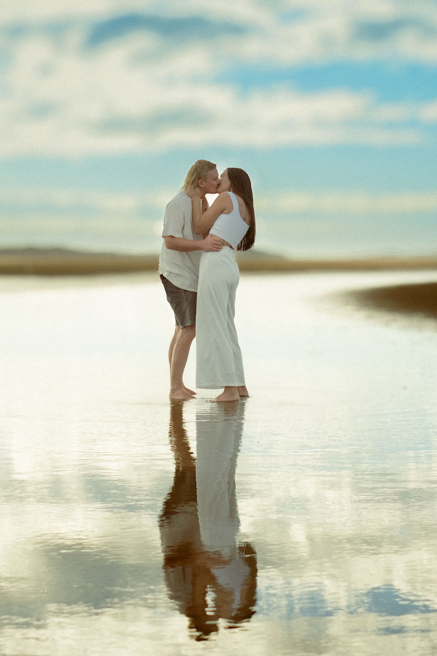 A romantic beach photoshoot with reflections in shallow water at sunset.