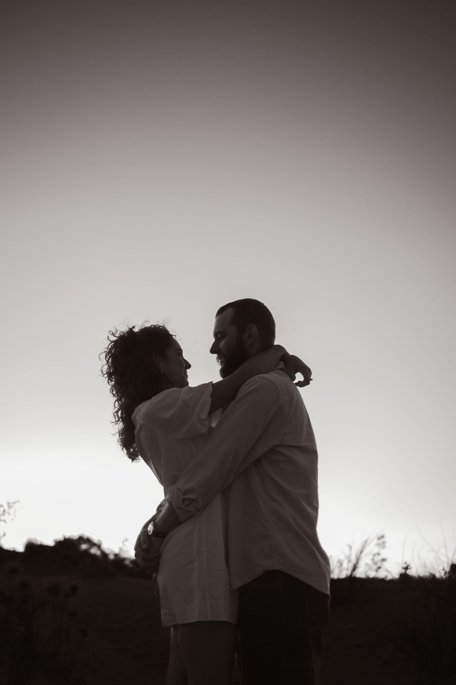 Dramatic black and white silhouette of a couple sharing a tender moment outdoors.