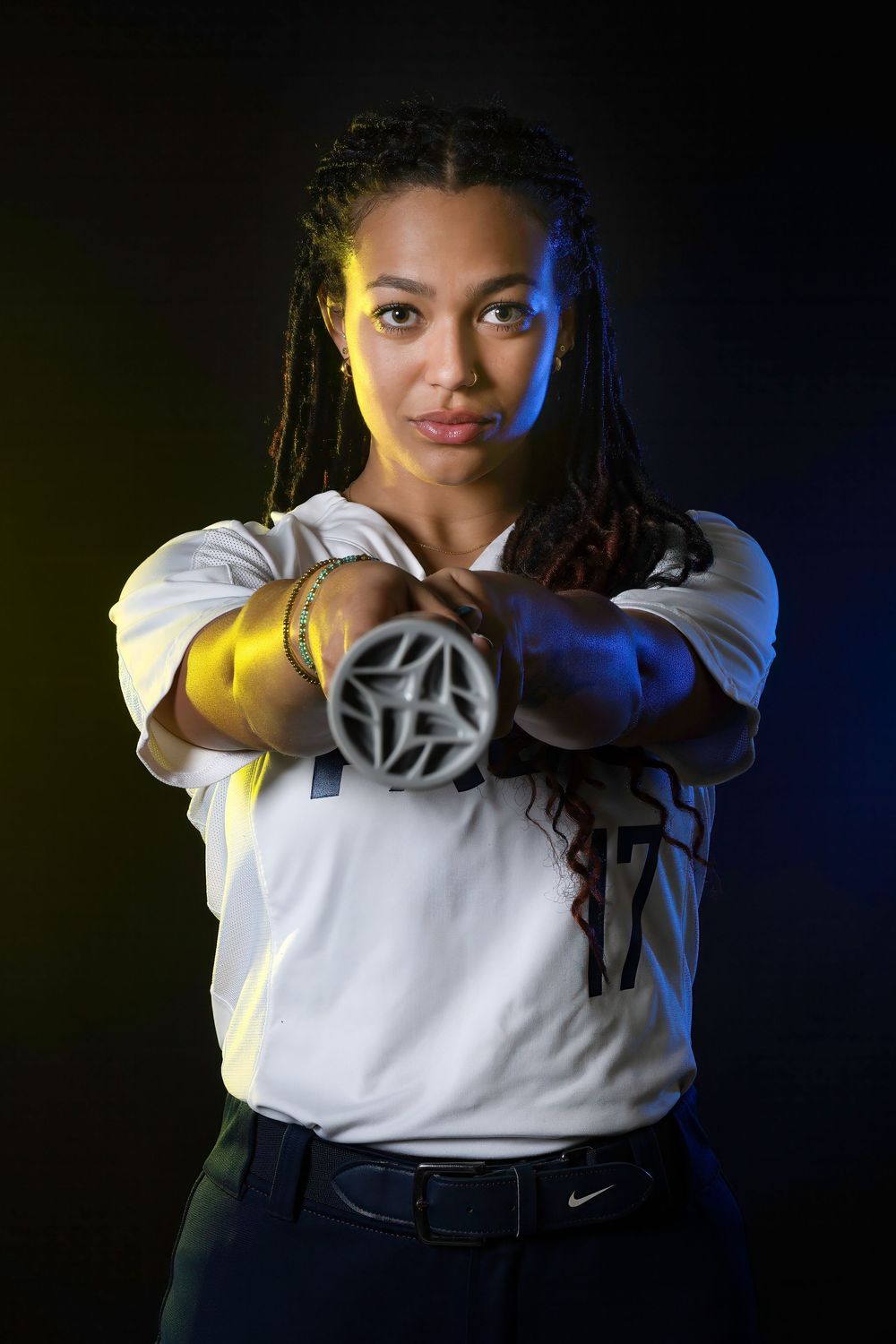 Athletic person in white shirt and dark pants poses with crossed arms against dramatic blue and yellow lighting.