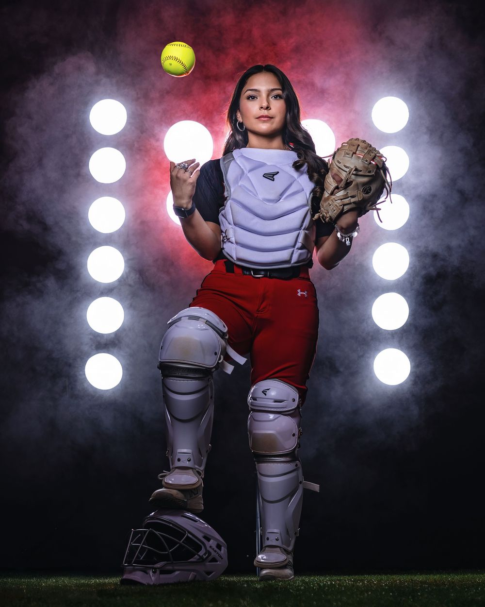 Dramatic sequence of softball catcher in gear catching a ball against dark background with bright white lights.
