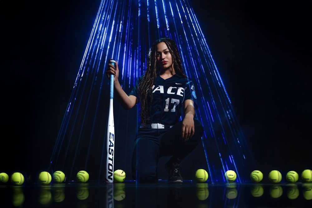 Tennis player poses with racket and tennis balls against dramatic blue lighting effect in dark setting.