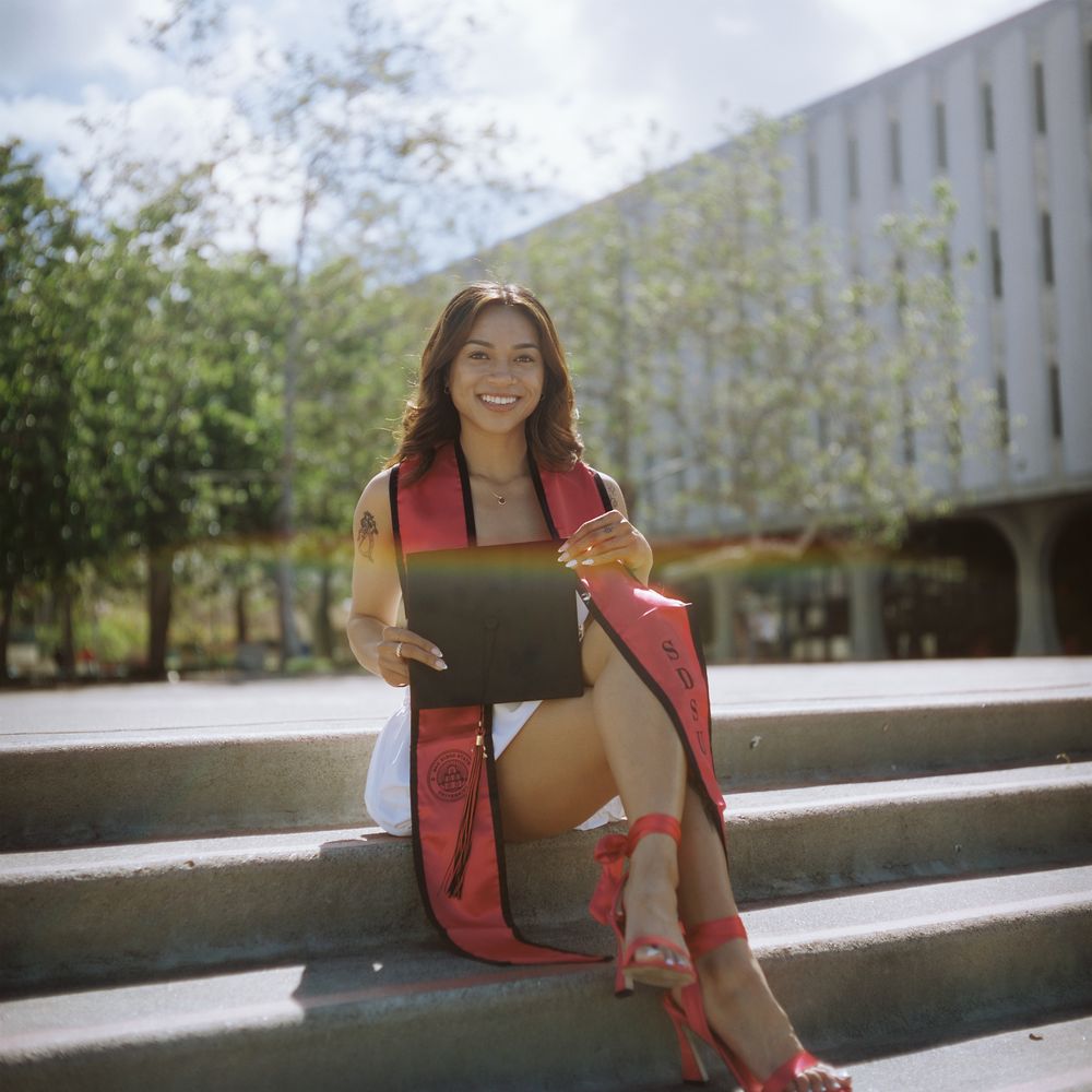 A young woman sits on a staircase, posing for a camera. A slight rainbow refracts off of the camera lens making a beautiful foreground