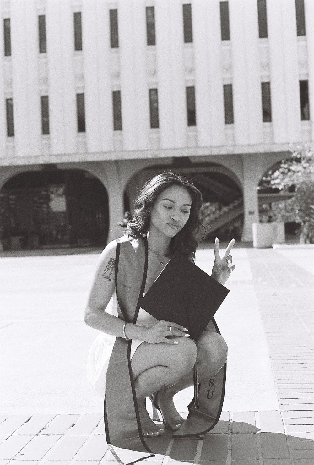 A young woman throws up a peace sign in a black and white photo as she crouches down in front of the camera