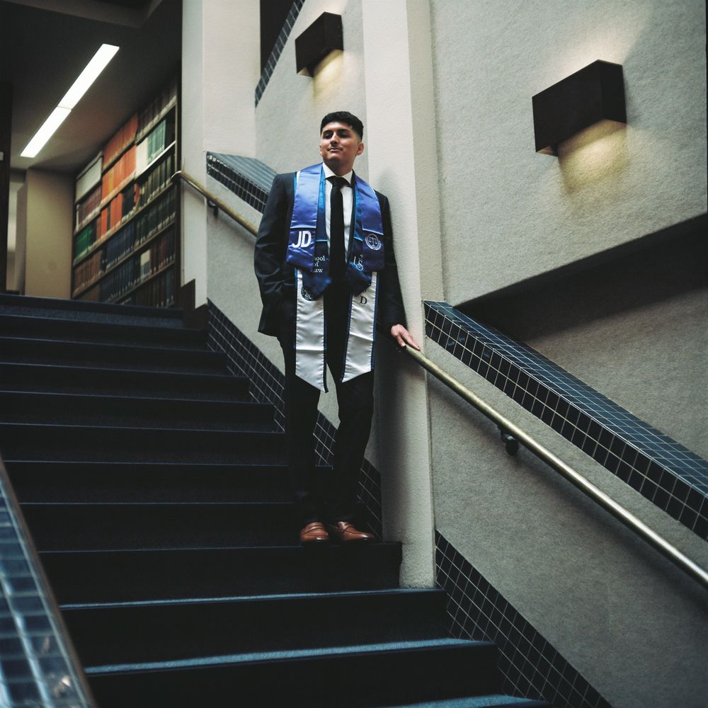 A young man poses in a building leaning on a banister on top of a staircase
