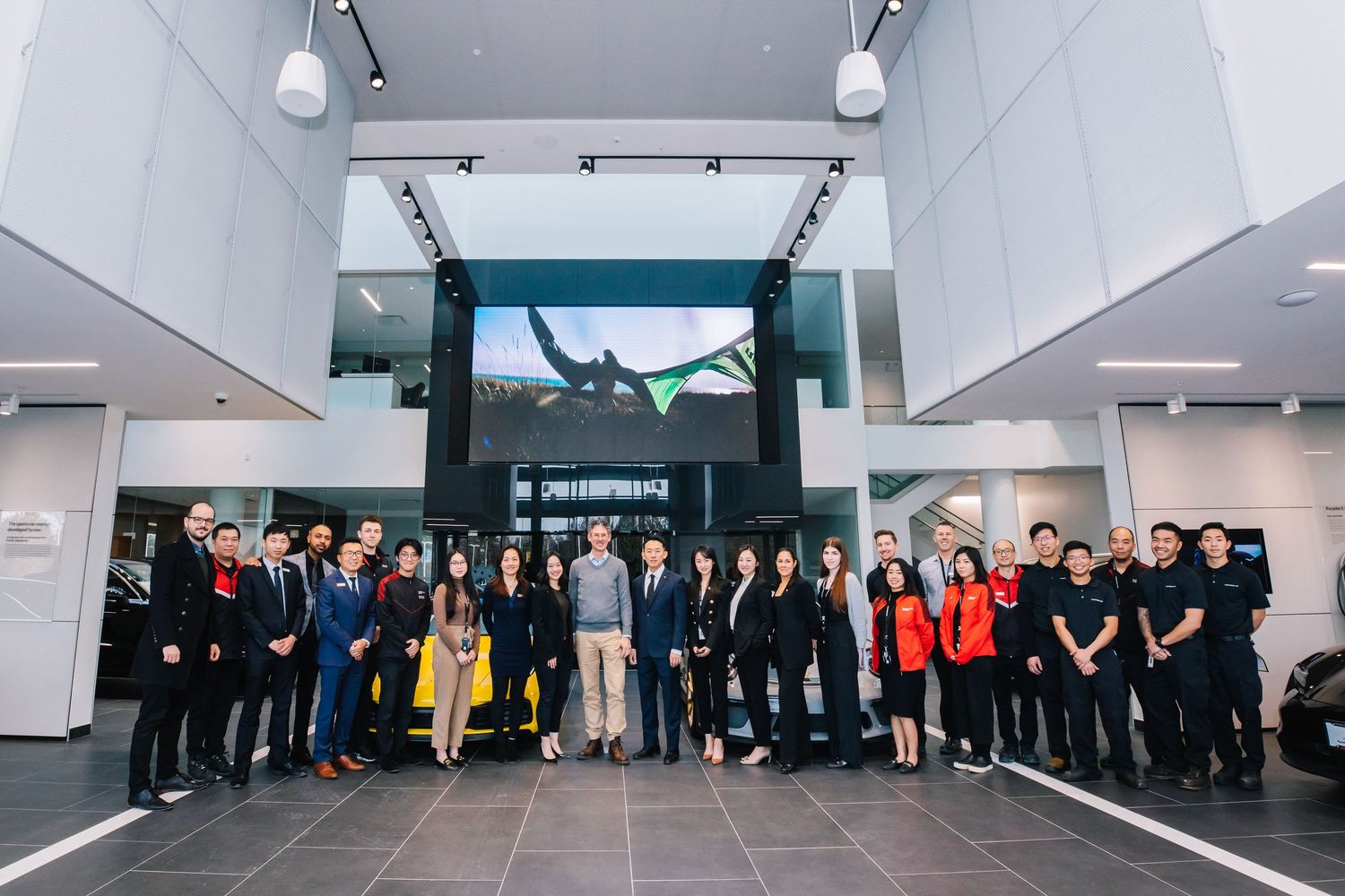 Large group of business professionals gathered in a modern corporate lobby with bright lighting and displays.