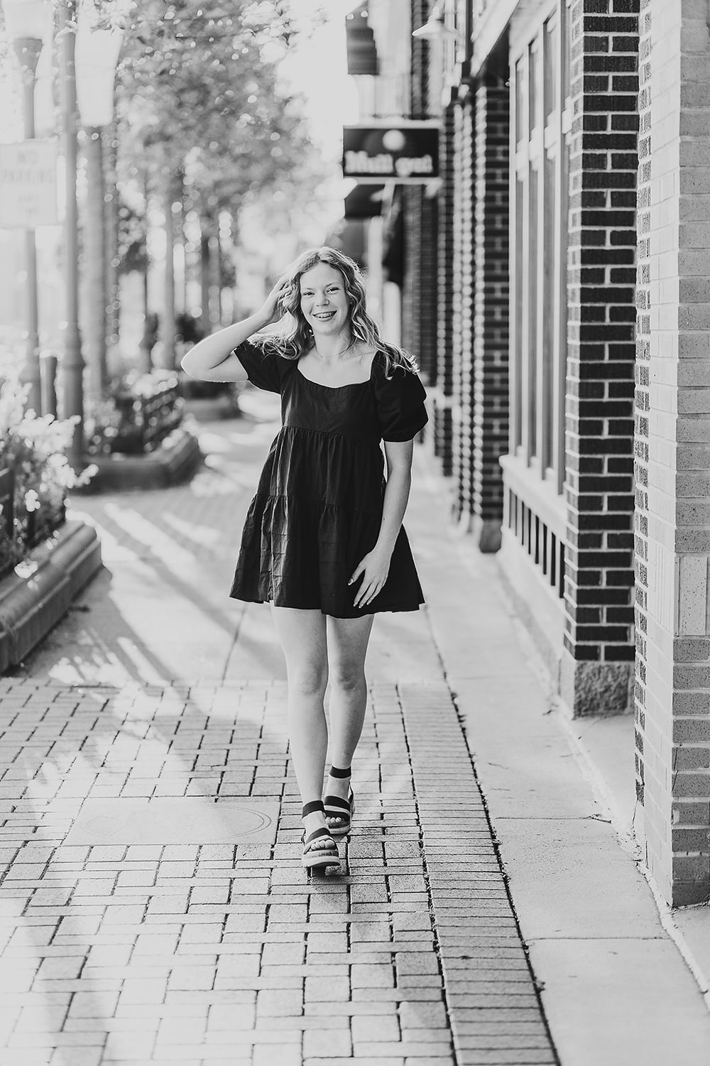 A series of four black and white photos showing someone in a black dress walking along a brick sidewalk in an urban setting.
