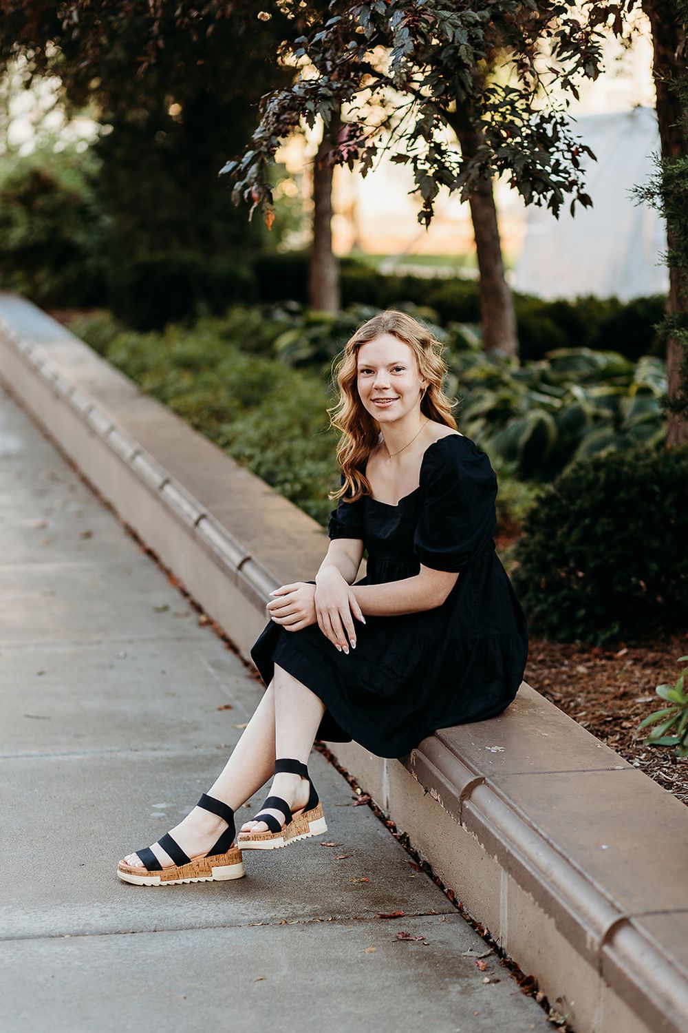 A black dress and sandals stand out in a casual outdoor photo session along a concrete curb at sunset.
