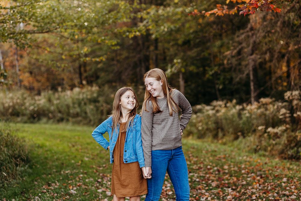 Two people enjoying a fall walk outdoors with autumn leaves scattered on the ground and trees in the background.