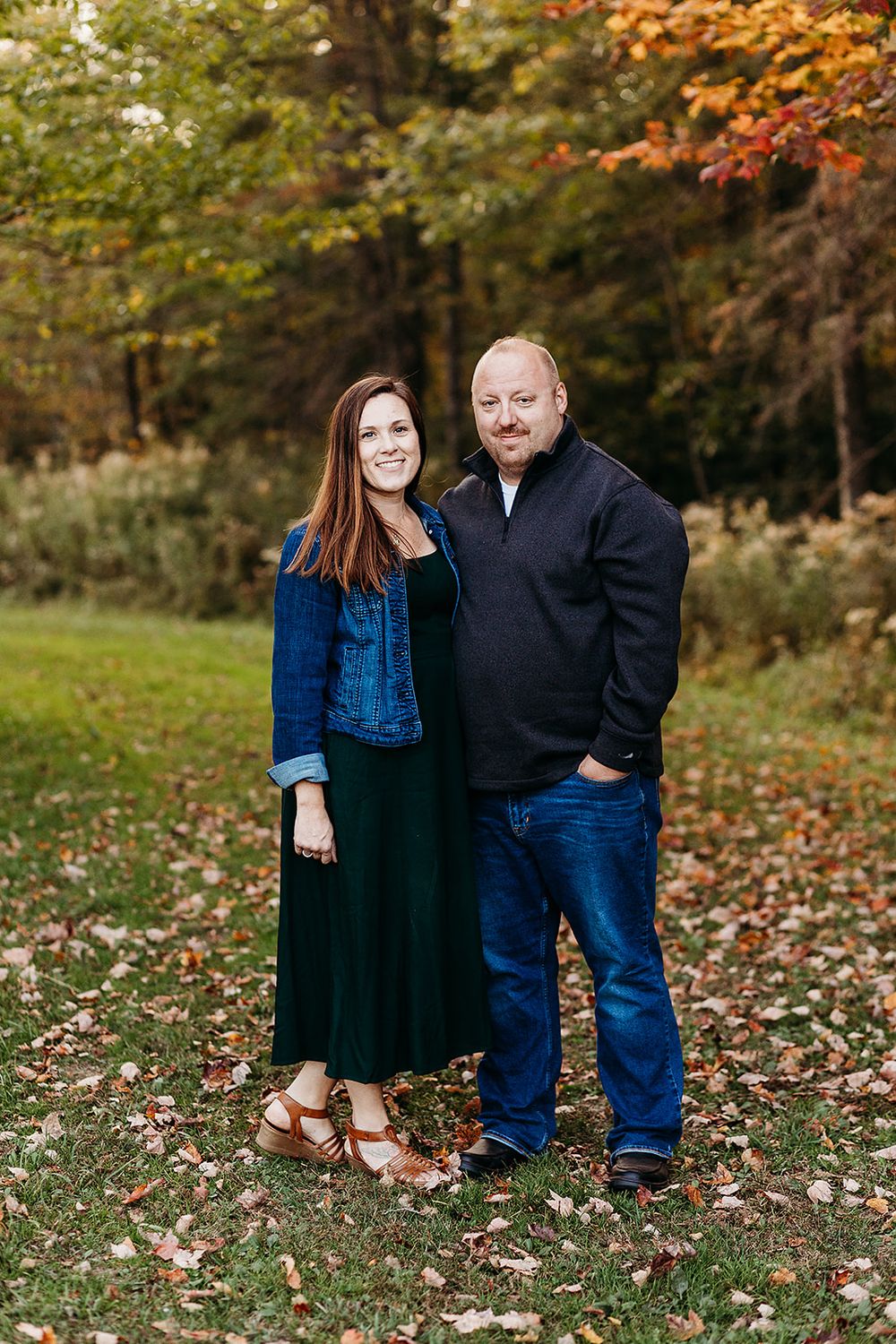 A couple poses together during an autumn outdoor photoshoot with fallen leaves on the ground.