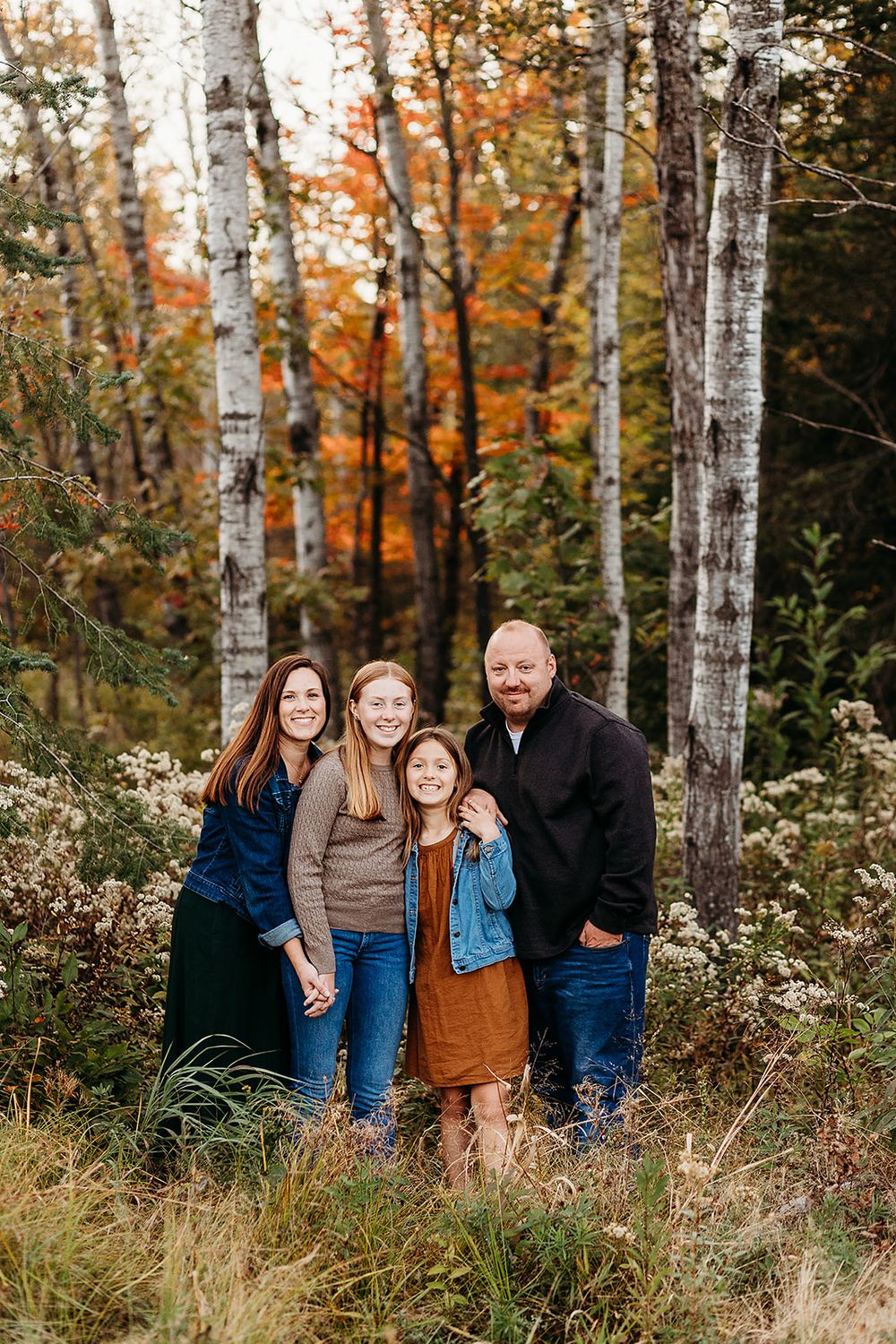 A group poses together surrounded by white birch trees and colorful autumn foliage in a scenic woodland setting.