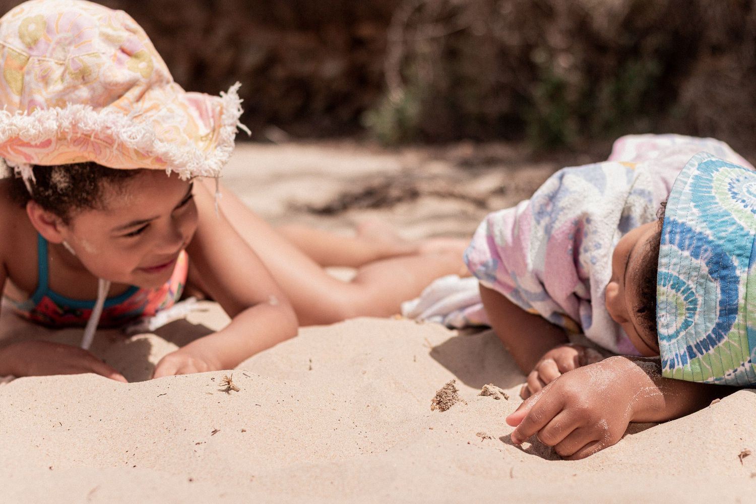 Children lie in sand at the beach while playing and exploring during a sunny summer day.