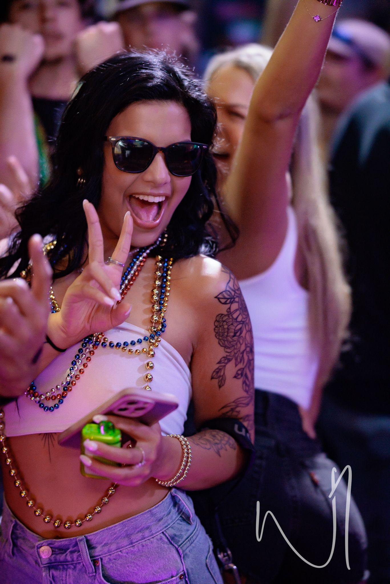 Party-goer in sunglasses flashing peace sign with beaded necklaces at festival.