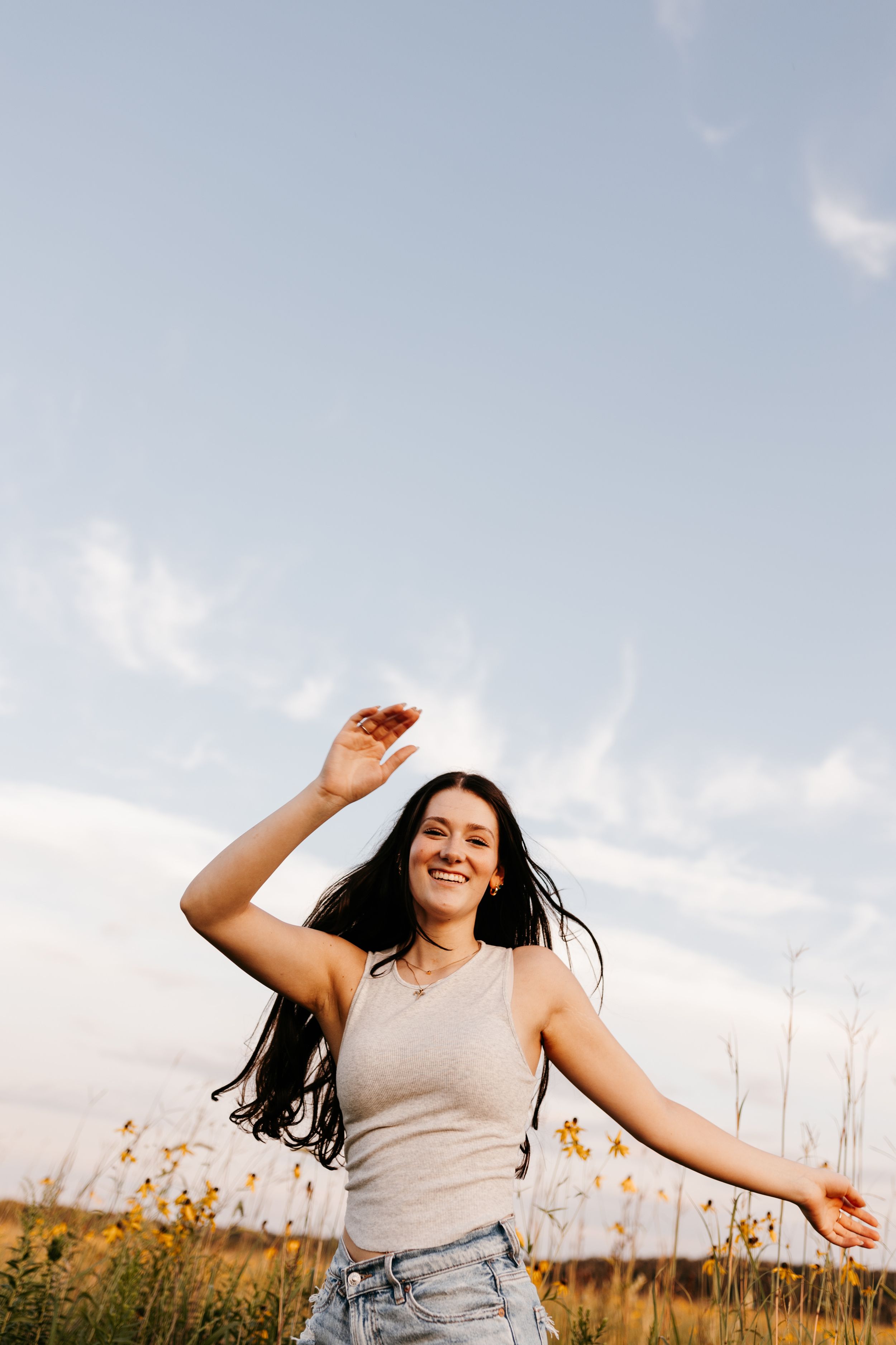 Person in a white dress sits peacefully in a golden field at sunset surrounded by wildflowers and tall grass.
