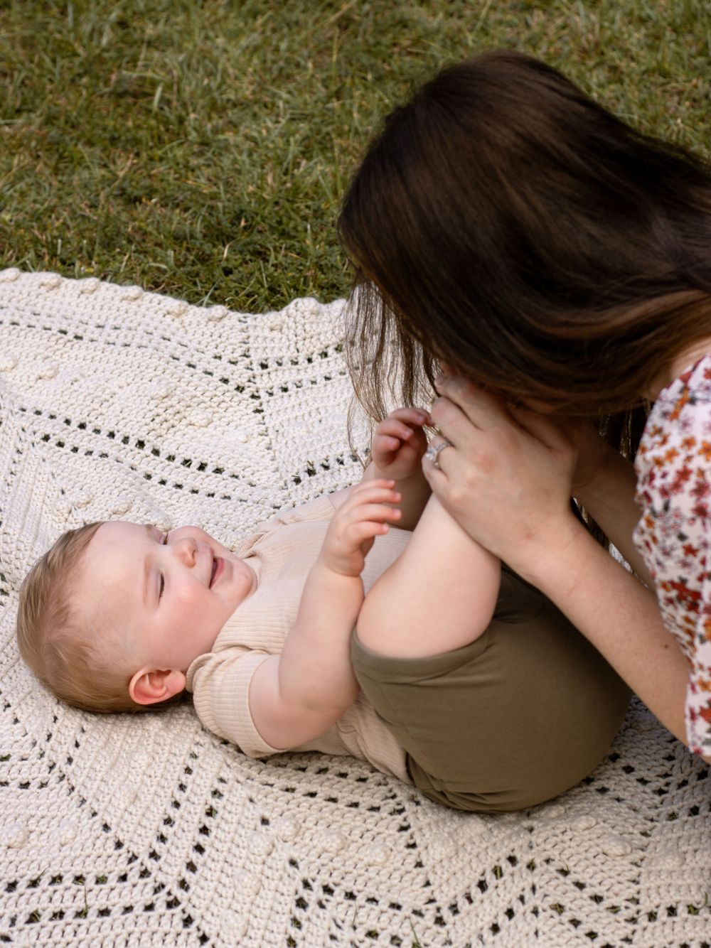 A tender moment between parent and baby lying on a crocheted blanket outdoors.