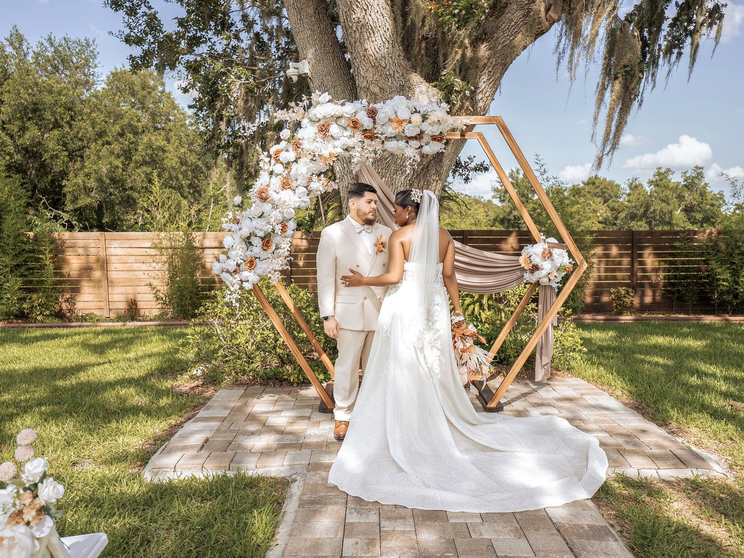A couple in wedding attire poses beneath a stone archway with lush greenery and dramatic lighting in a garden setting.