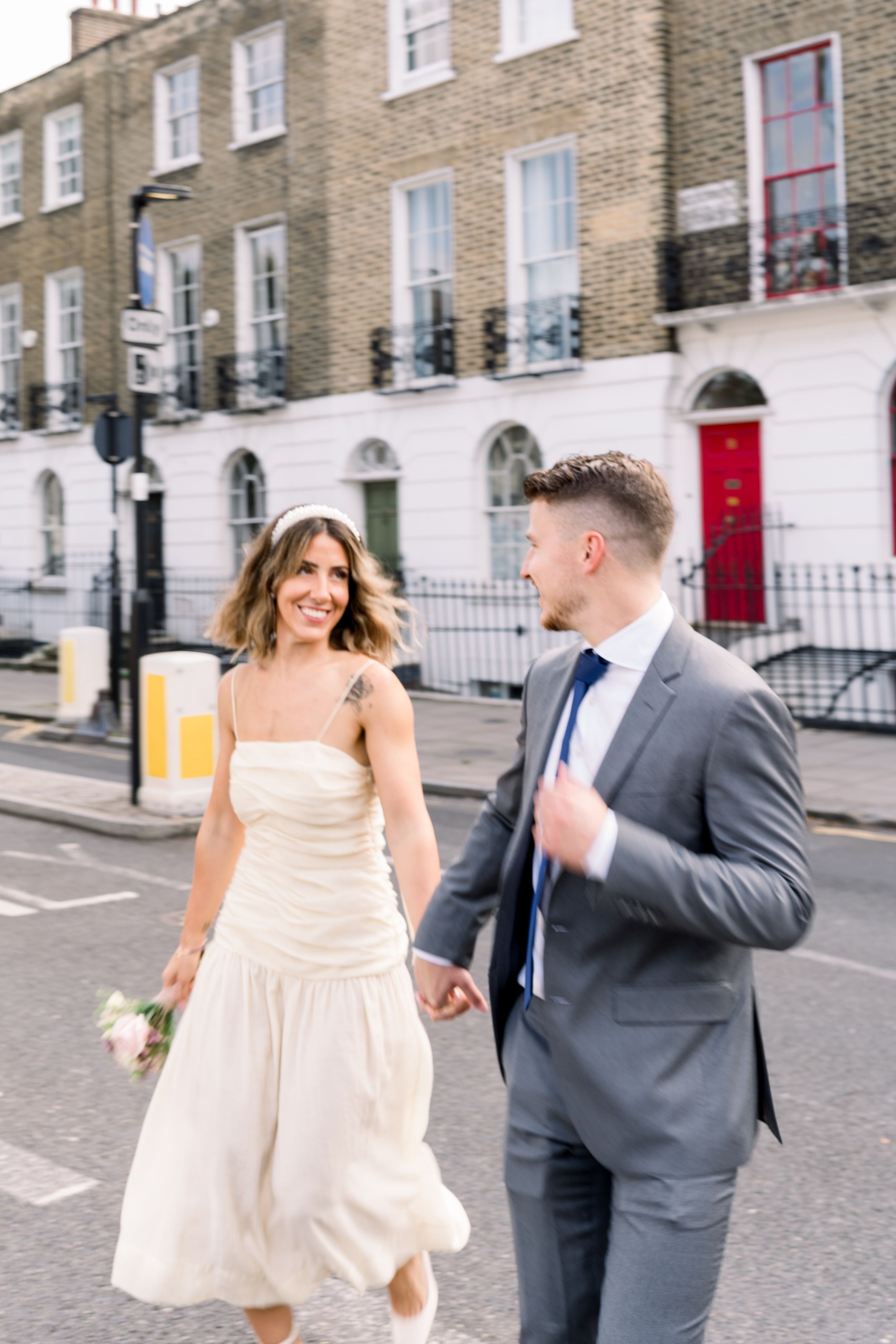 Bride and groom running through the streets just outside Islington Town Hall, smiling at each other after their relaxed London elopement.