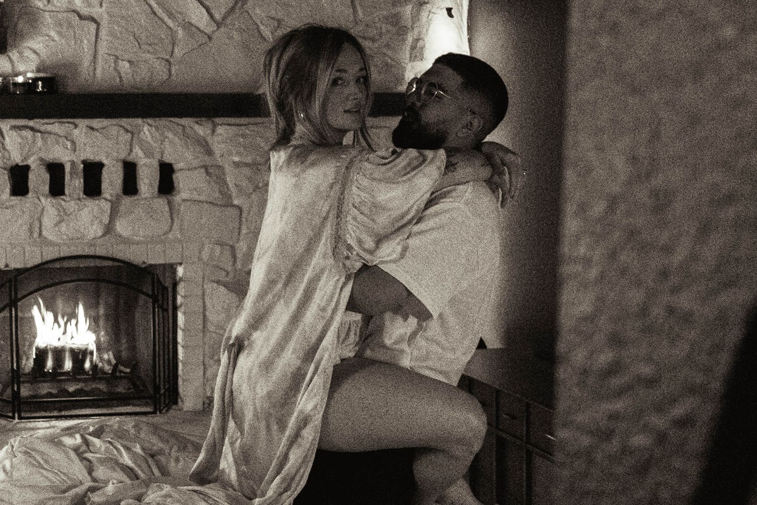 Romantic black and white photo of couple by fireplace in intimate moment.