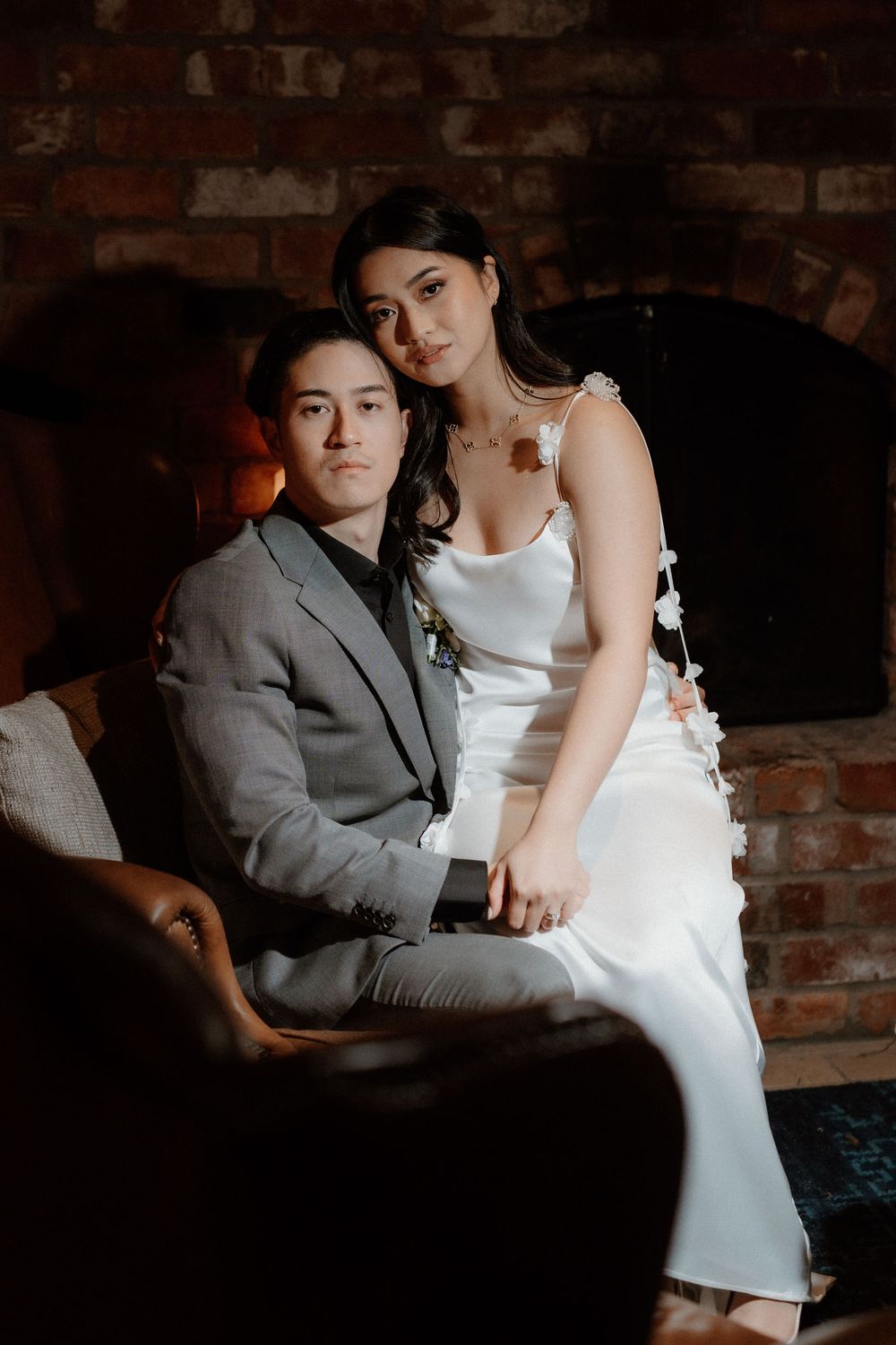 A romantic wedding portrait in a dimly lit room with exposed brick walls, featuring a couple in elegant attire.