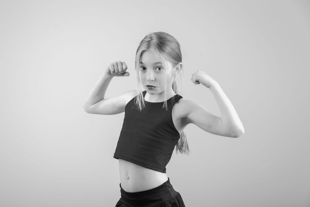 A person in workout attire flexes their muscles while striking a strong athletic pose against a gray background.