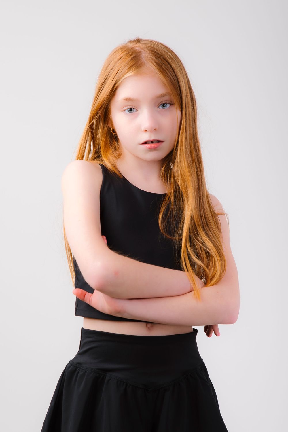 A figure in a black outfit with flowing red hair poses against a light background with arms crossed.