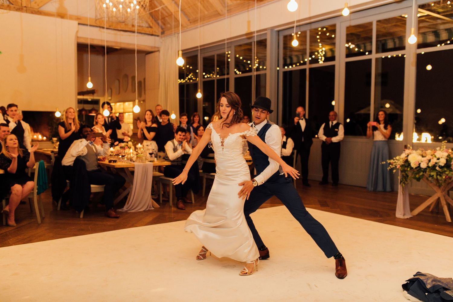 Two dancers perform a romantic ballroom dance during an evening reception in an elegant venue with candlelit tables.