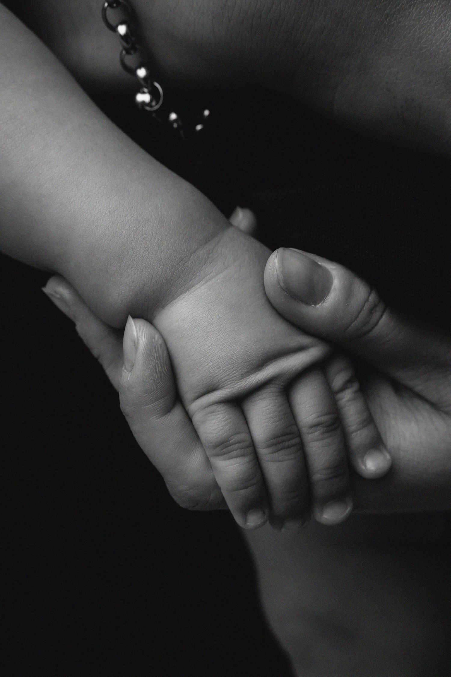 A close-up black and white image of hands holding each other tenderly, showing a gentle connection in the dark.