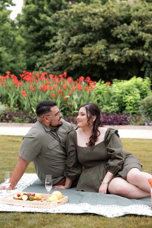 A romantic couple enjoys a spring picnic on a blanket with red tulips blooming in the garden background.