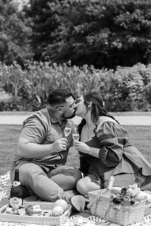 A romantic picnic scene at a garden with wine glasses and a wicker basket filled with snacks on a blanket.