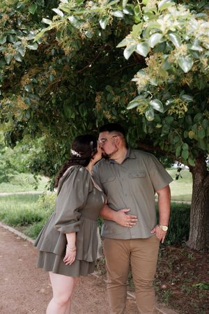 Romantic couple sharing tender moment under lush green tree canopy on garden path.