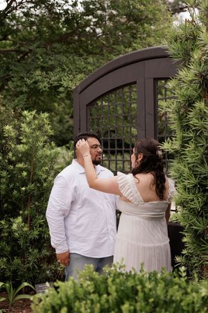 A loving moment shared between a couple by a decorative black gate in a garden setting.