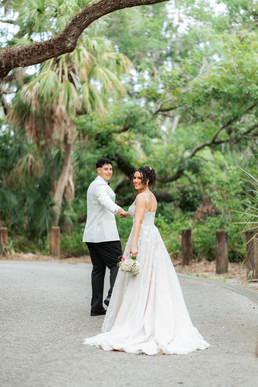 Wedding couple shares a romantic moment on a palm tree-lined path in a lush garden setting.