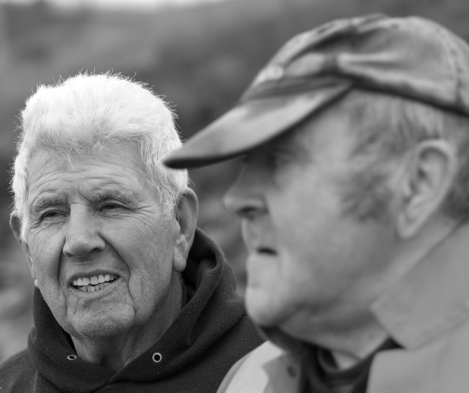 Black and white photo of two elderly men having a conversation while wearing casual outdoor clothing.