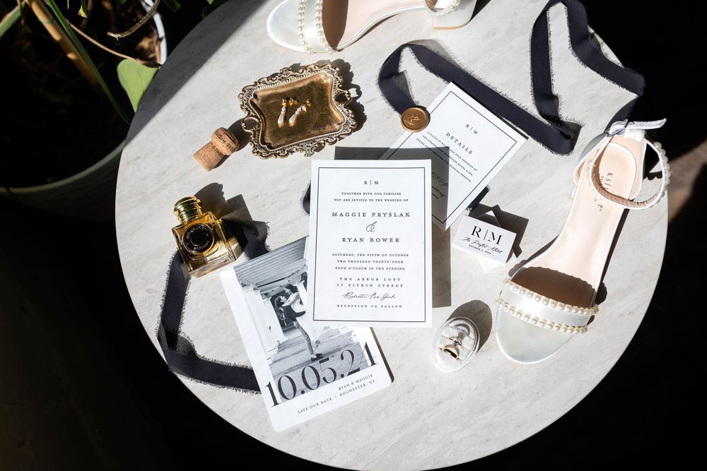 Wedding accessories including white heels, invitation card, and decorative details arranged on a round marble surface.