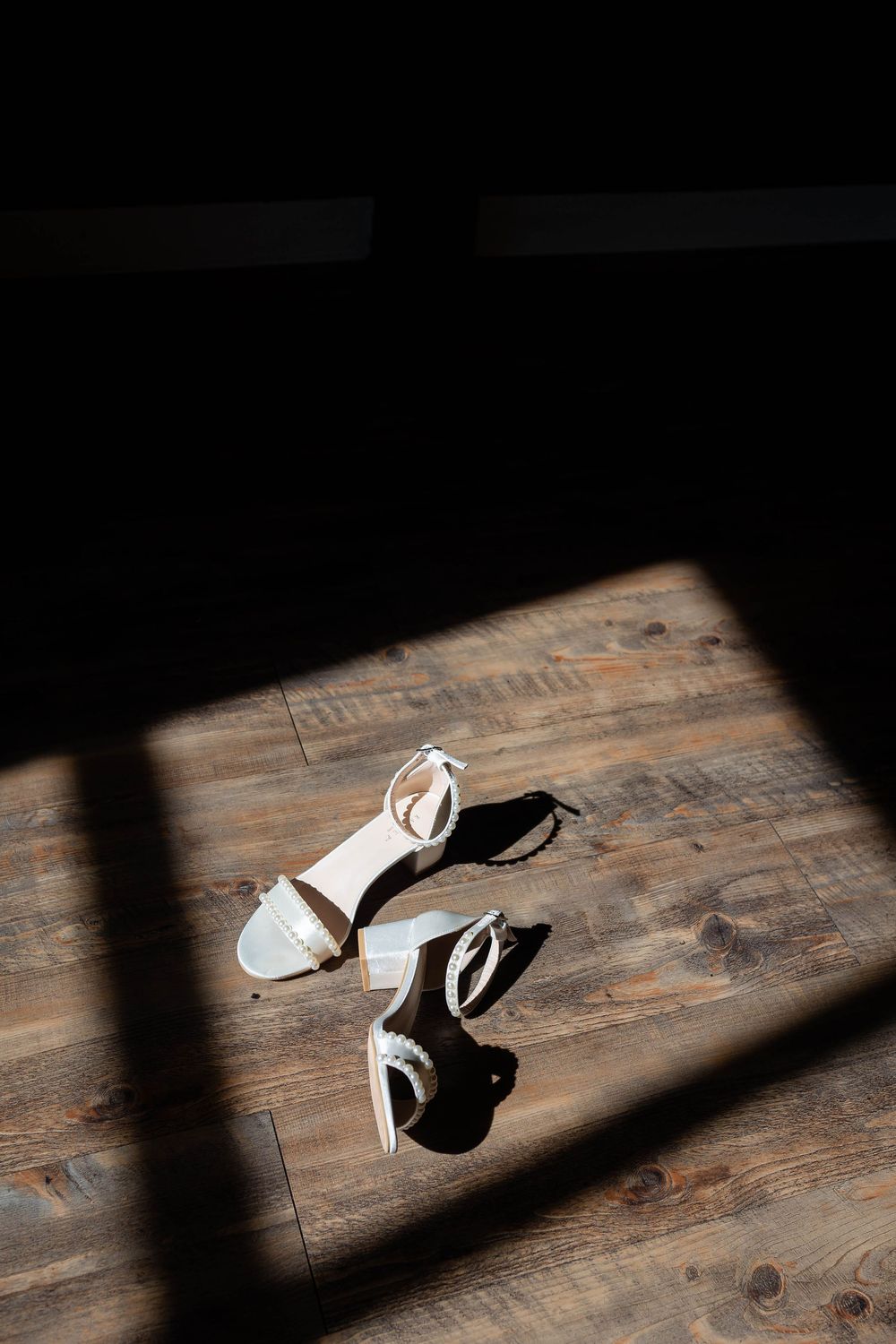 White sandals on a dark wooden floor casting dramatic shadows in natural light through a window.