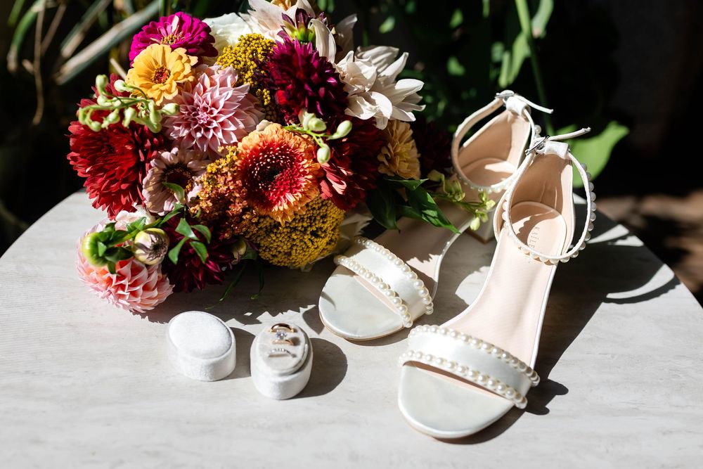 Elegant white bridal sandals next to a vibrant autumn-colored wedding bouquet with dahlias and mixed flowers.