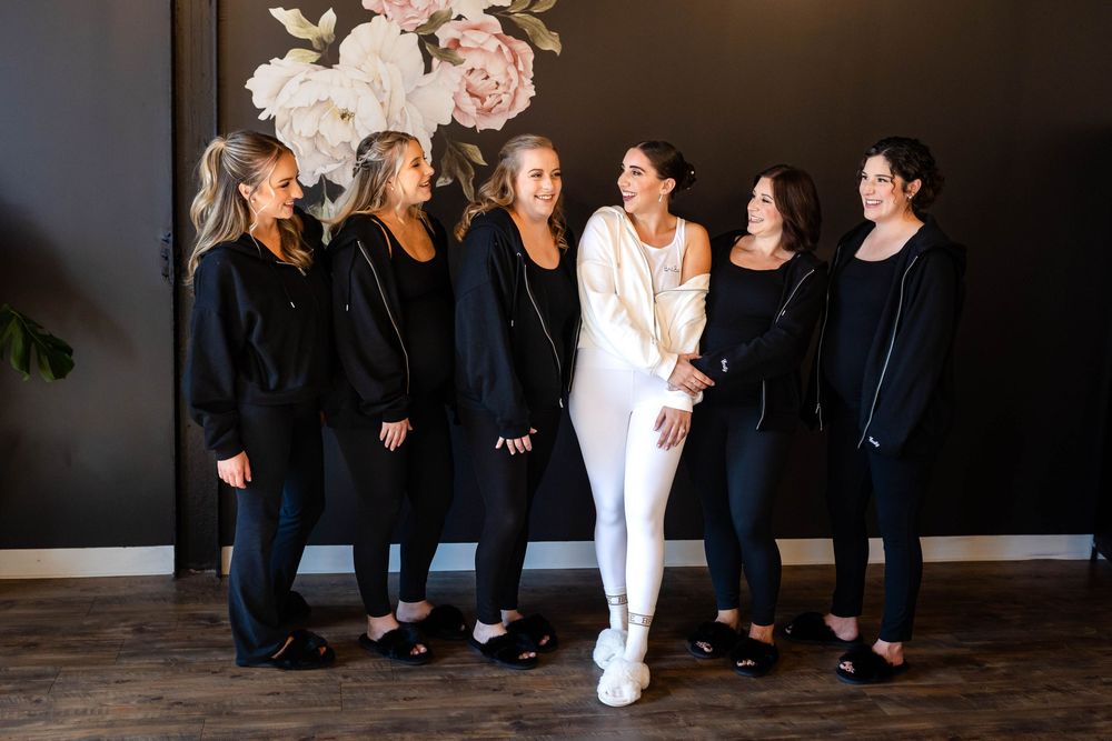 A person in white stands with a group in black outfits on a dark background with floral decor.