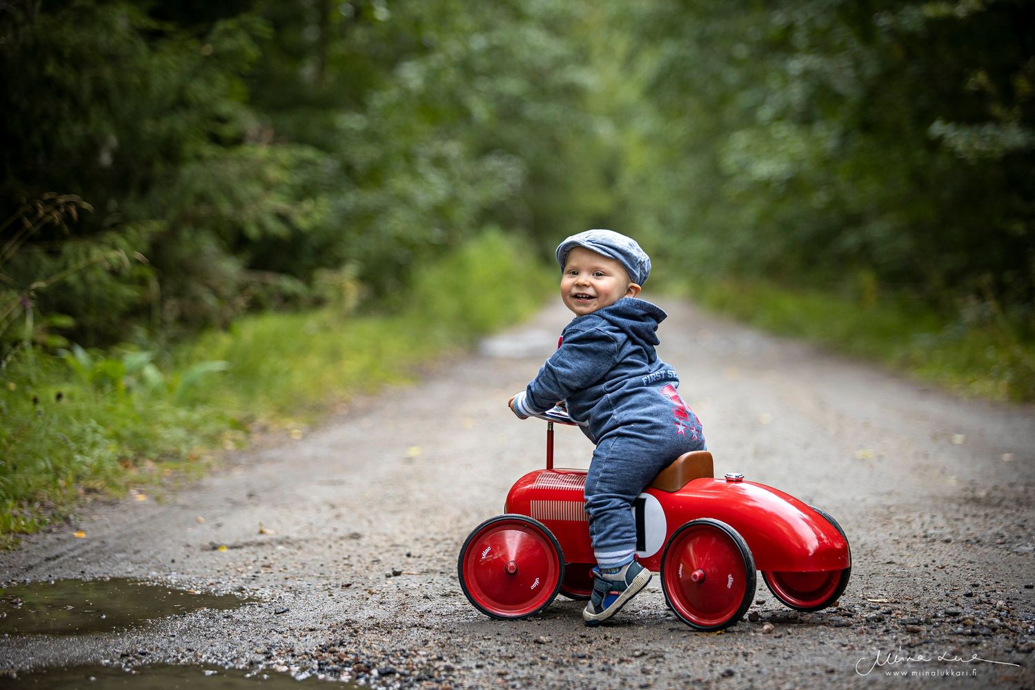 Farkkuasuun puettu lapsi istuu potkuauton päällä soratiellä.