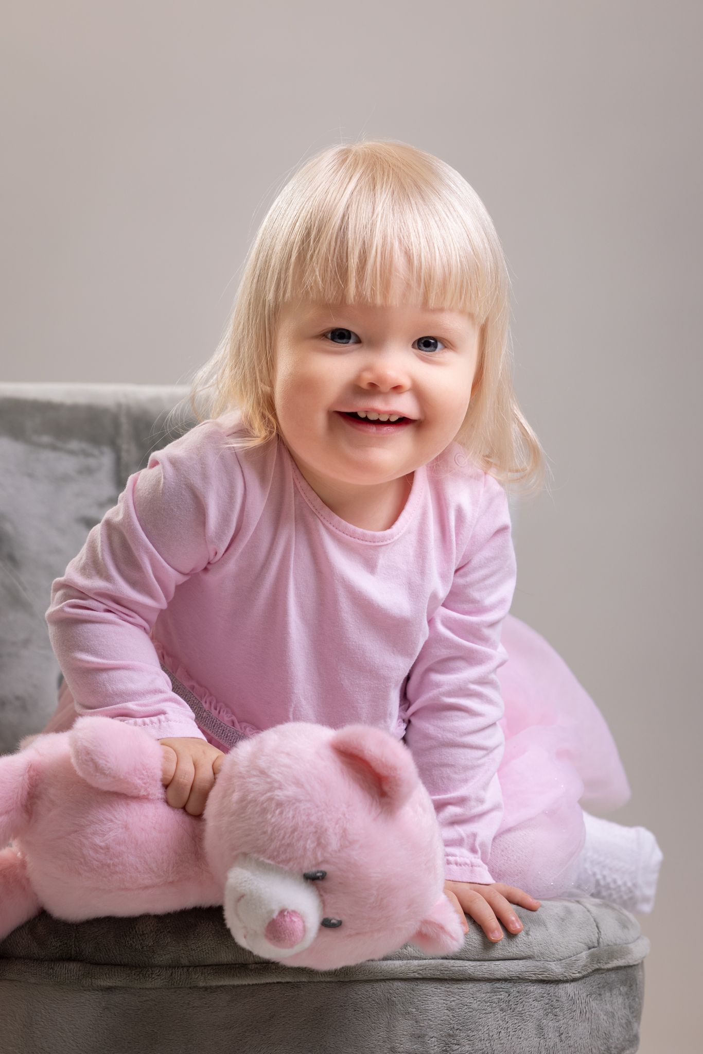 Pinkkiin puettu lapsi vaaleanvihreässä nojatuolissa, sylissään pinkki pehmonalle.