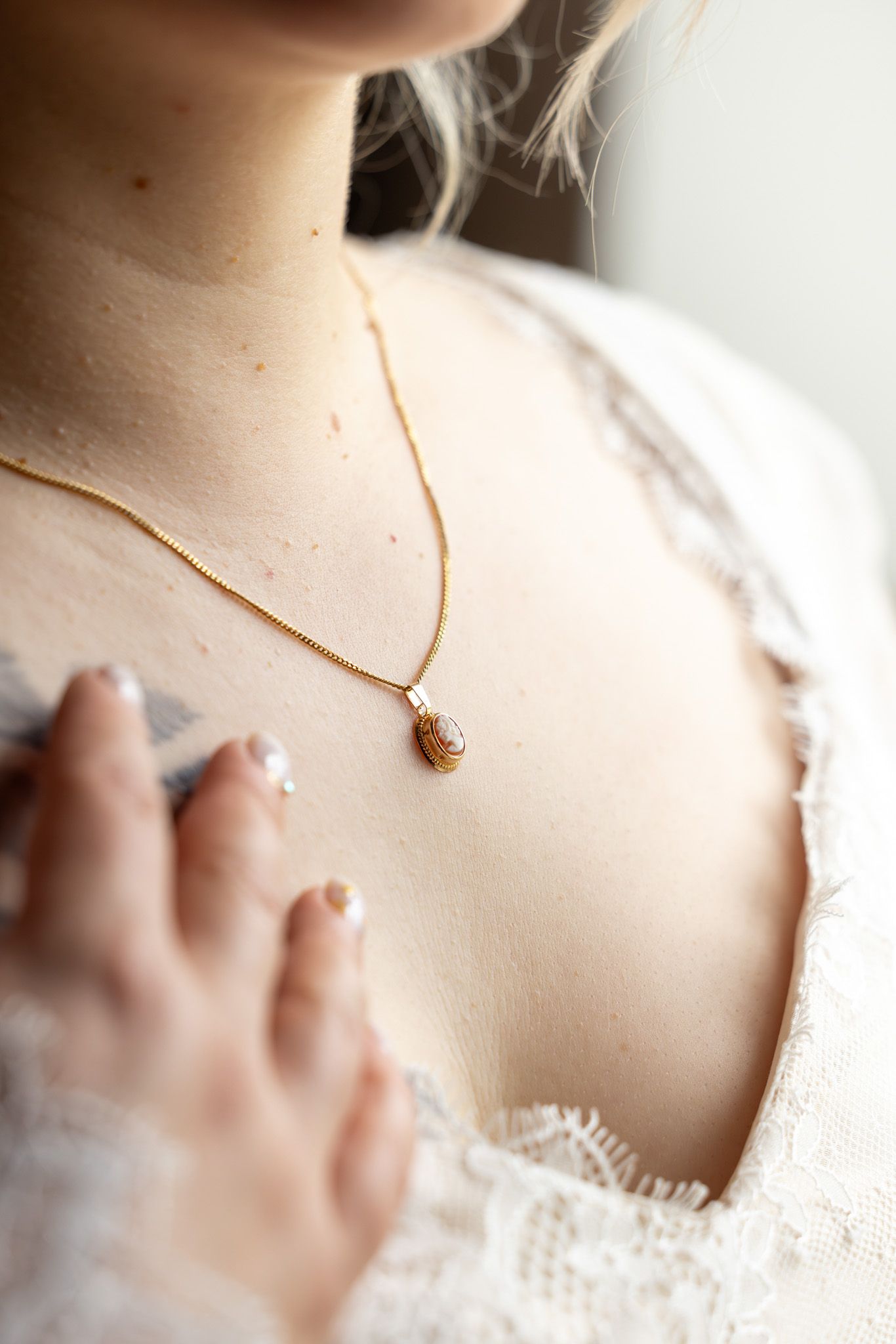 Close-up of a gold teardrop pendant necklace worn by a woman in white lace dress.