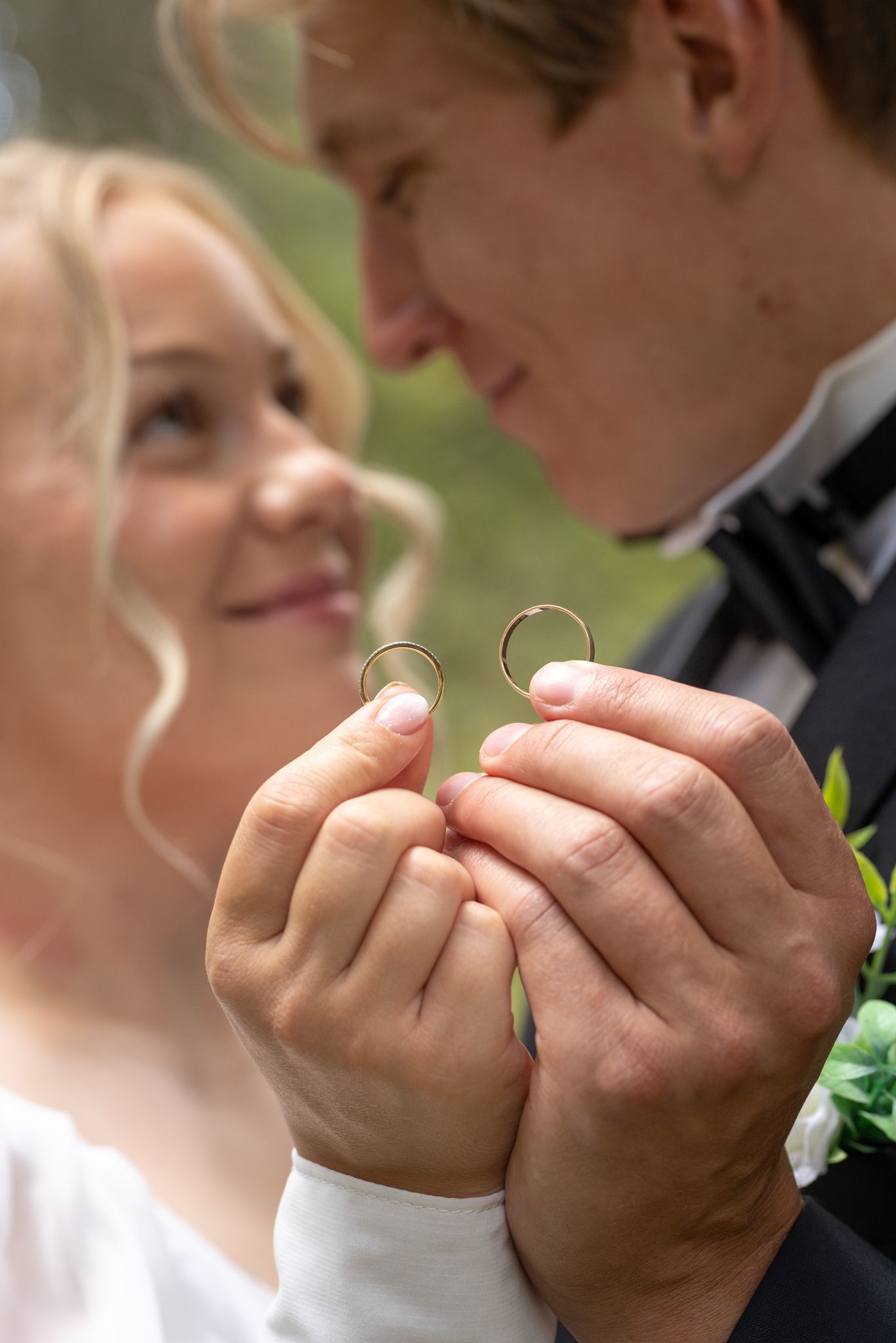 Smiling newlyweds holding up two gold wedding rings together on their wedding day.