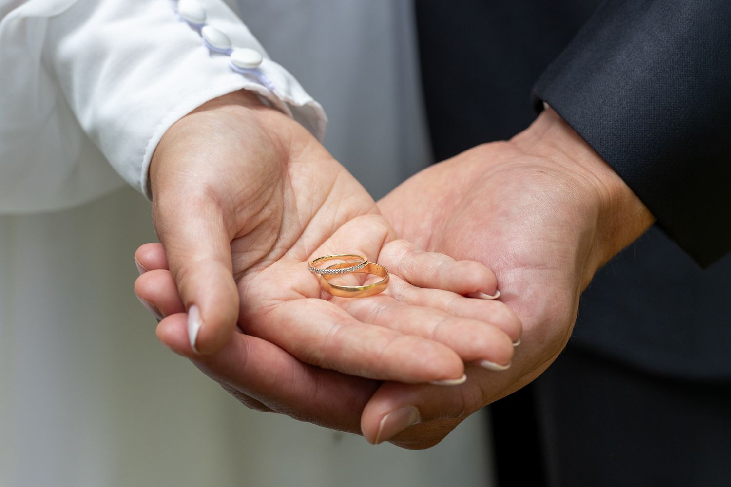 Two hands holding gold wedding rings together, symbolizing marriage and commitment in a wedding ceremony.