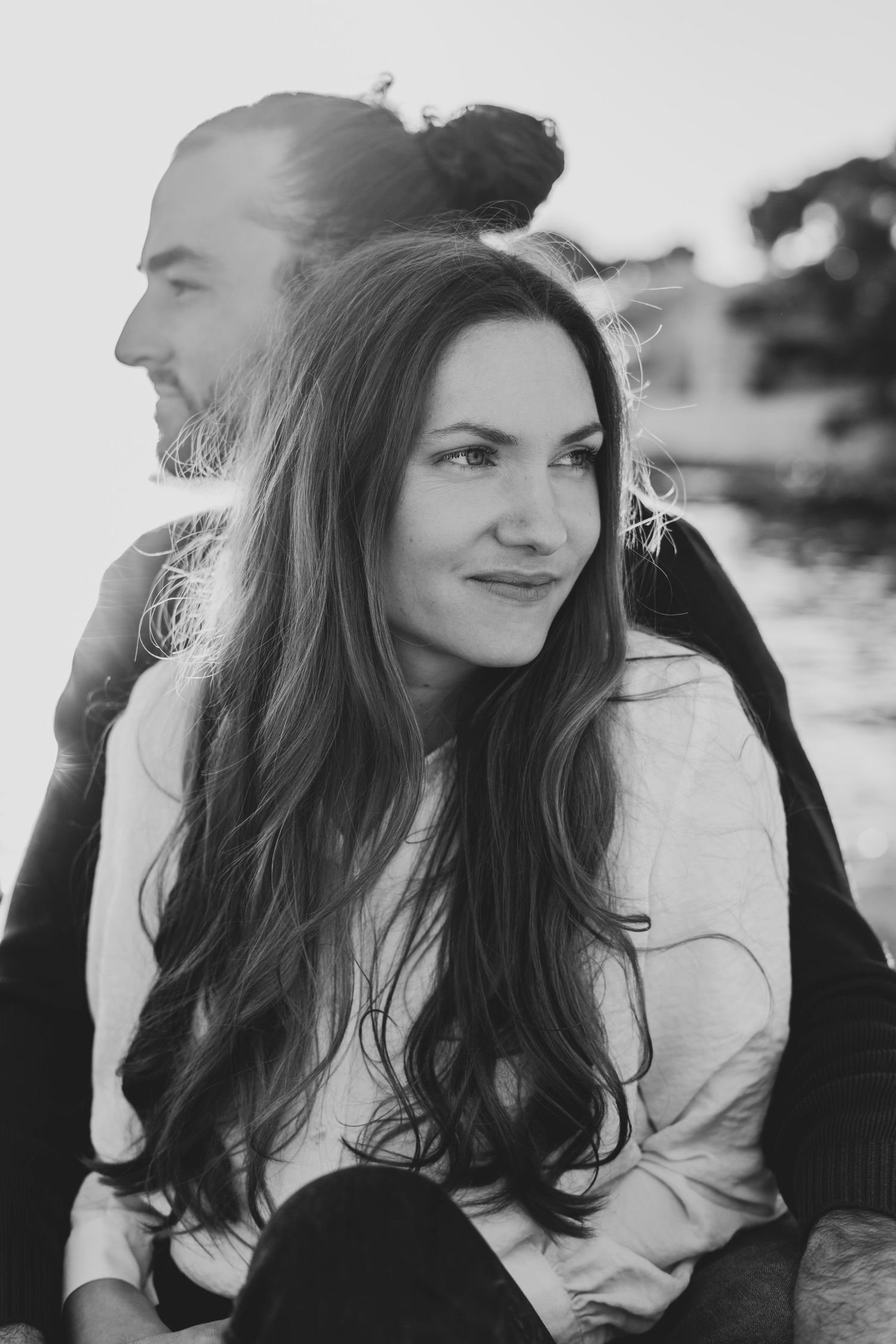 Black and white portrait of a couple outdoors, with long dark hair and a beard, in natural lighting.
